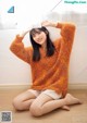 A woman sitting on the floor wearing an orange sweater.