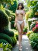 A woman in a white bikini walking down a path in a garden.