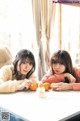 Two young women sitting at a table with oranges.