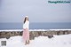 A woman standing on a wall in the snow near the ocean.