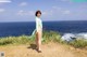 A woman in a green dress standing on a cliff overlooking the ocean.