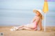 A woman in a bikini and hat sitting on the beach.