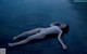 A naked woman laying on the ground in the water.